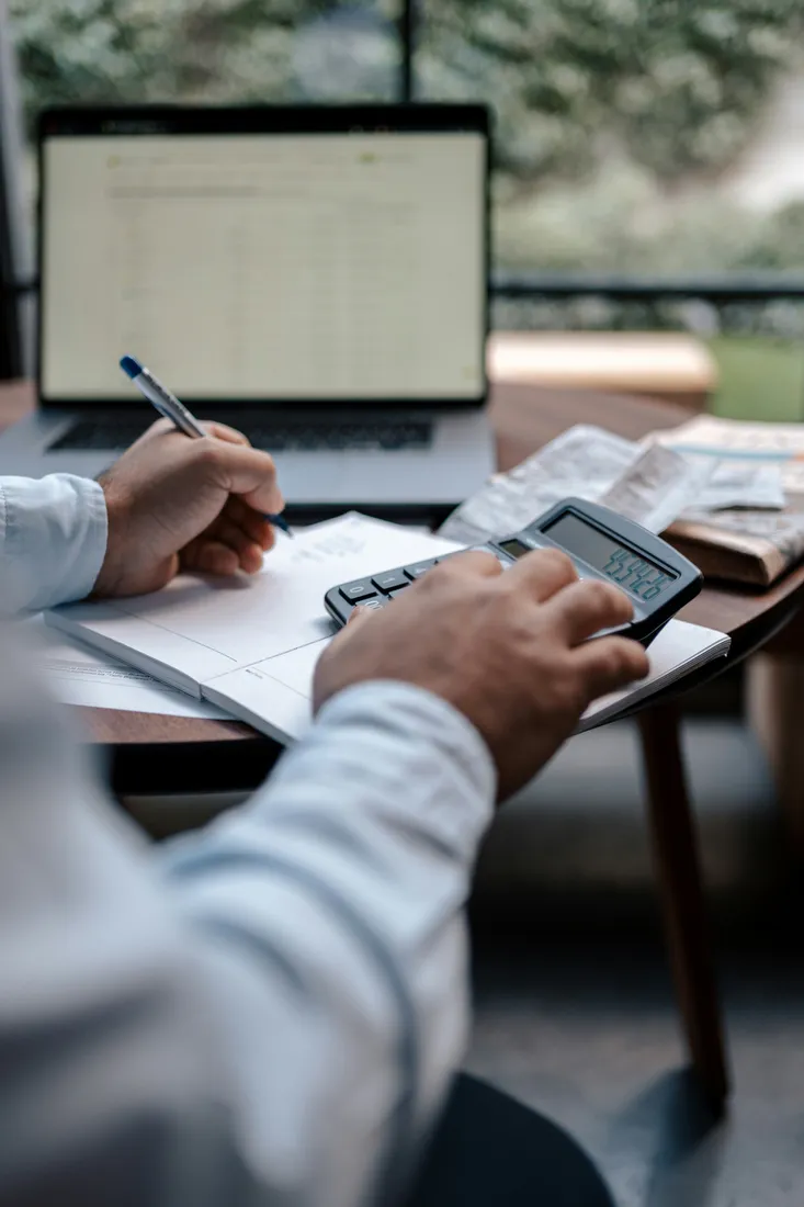 Bookkeeper reviewing monthly records with a calculator and laptop